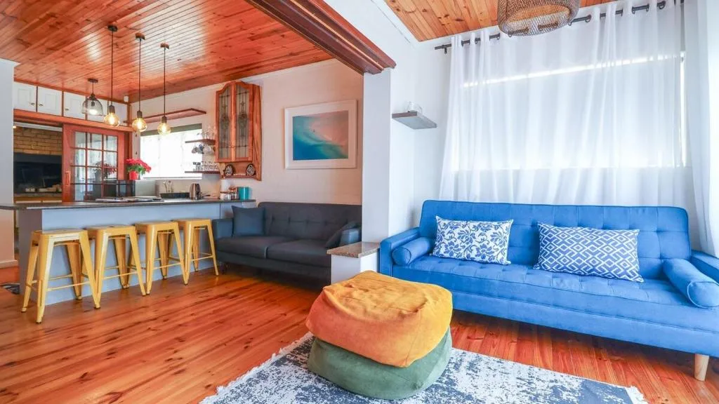 Bright open-plan lounge with blue sofa, colorful poufs, and wooden finishes