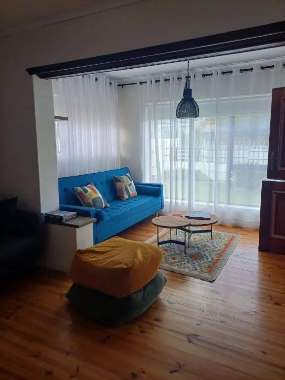 Bright lounge with blue sofa, poufs, and large windows overlooking garden