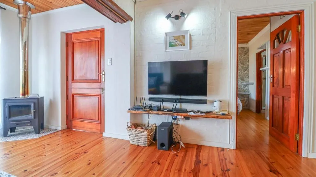 Open-plan lounge with wall-mounted TV, wooden floors, fireplace, and red doors