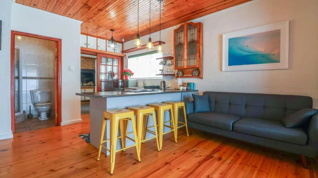 Modern lounge with dark sofa, open-plan kitchen, wooden ceiling, pendant lighting