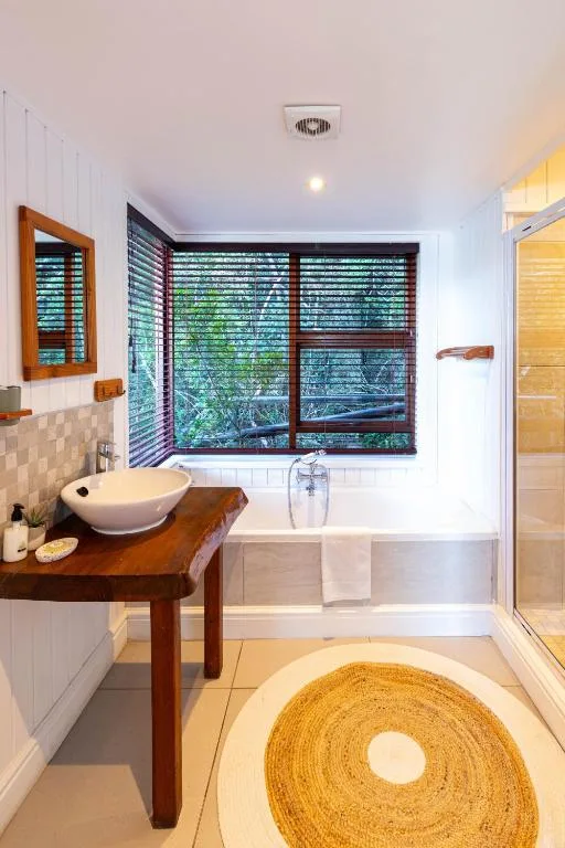 Modern bathroom with wooden vanity, white vessel sink, and soaking tub with garden views