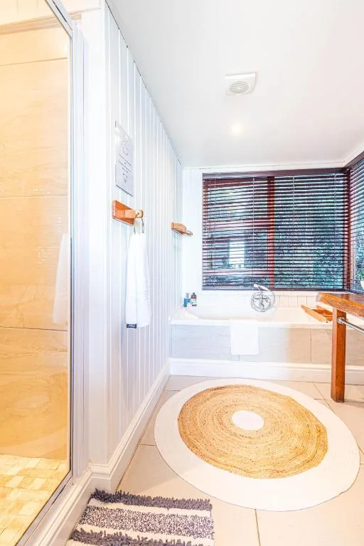 Bright bathroom with shower enclosure, bathtub, and woven circular floor mat