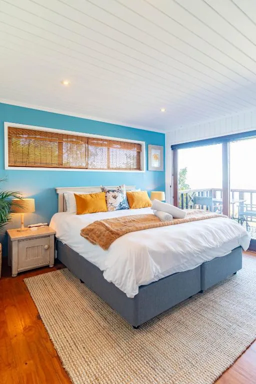 Bright bedroom with blue accent wall, queen bed, and ocean view balcony access