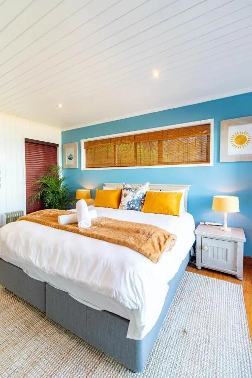 Bright bedroom with blue accent wall, queen bed, yellow pillows, and ocean artwork
