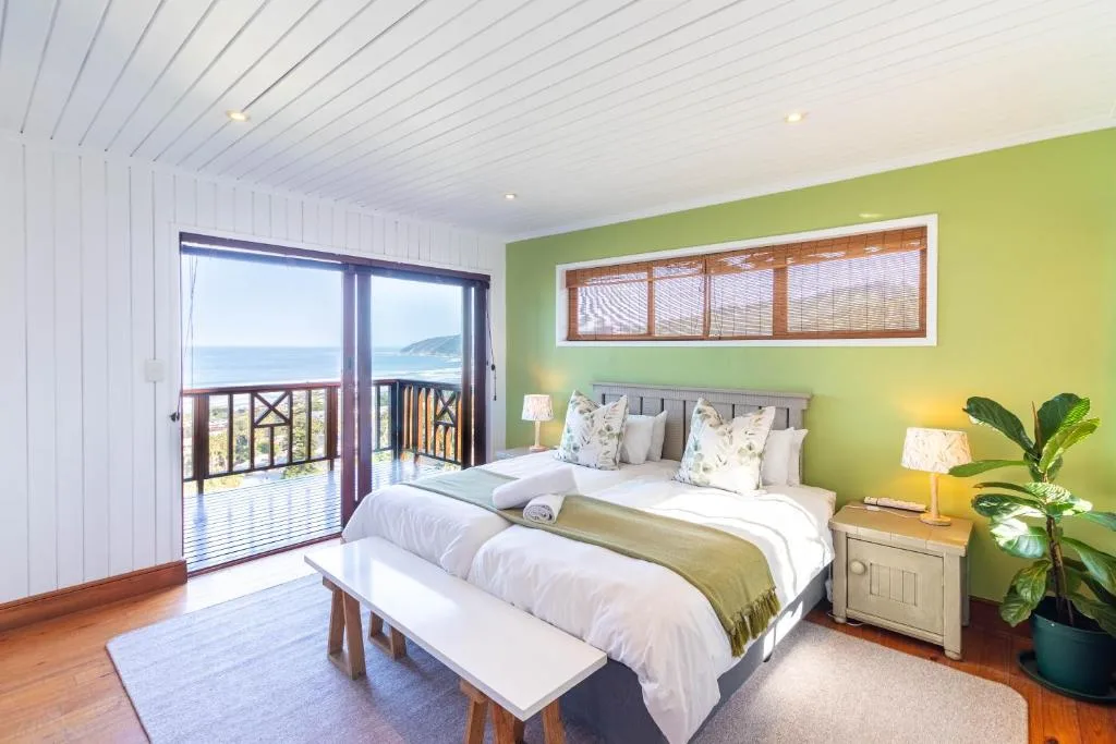 Bright green bedroom with ocean views through glass doors to deck