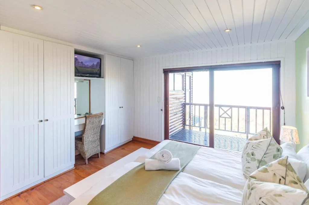 Bright bedroom with queen bed, deck access, and ocean views through glass doors