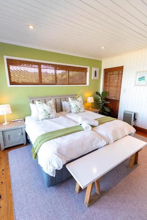 Bright bedroom with twin beds, green accent wall, wooden blinds, modern lighting