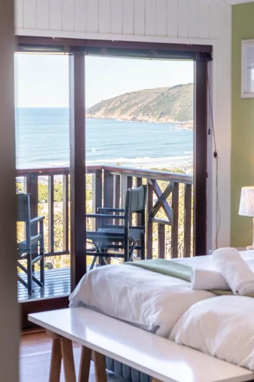 Bedroom with ocean view through glass doors and coastal cliffs beyond