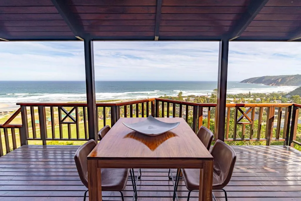 Covered wooden deck with dining table overlooking ocean and coastline