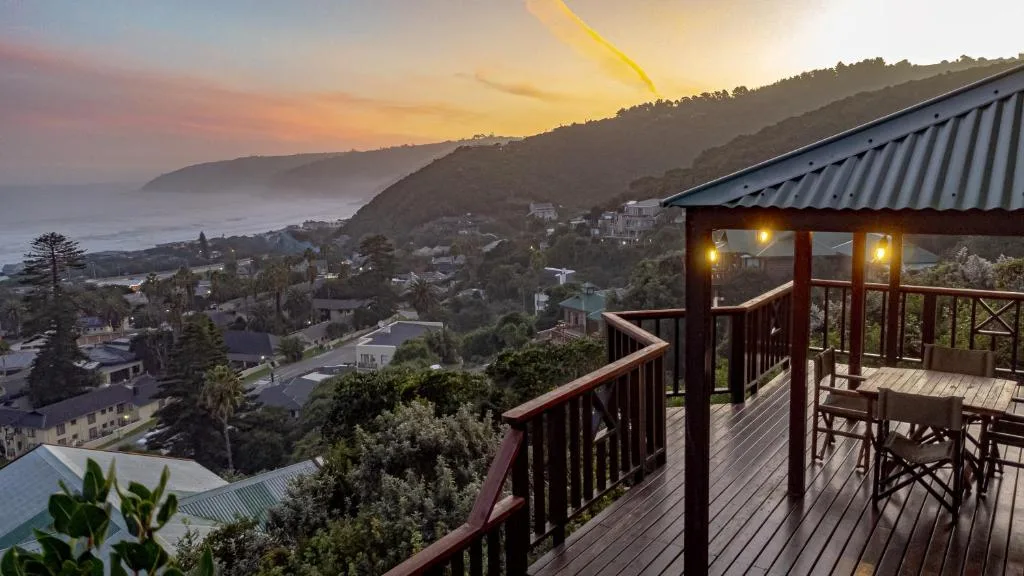 Wooden deck with ocean and mountain views at sunset, coastal town below