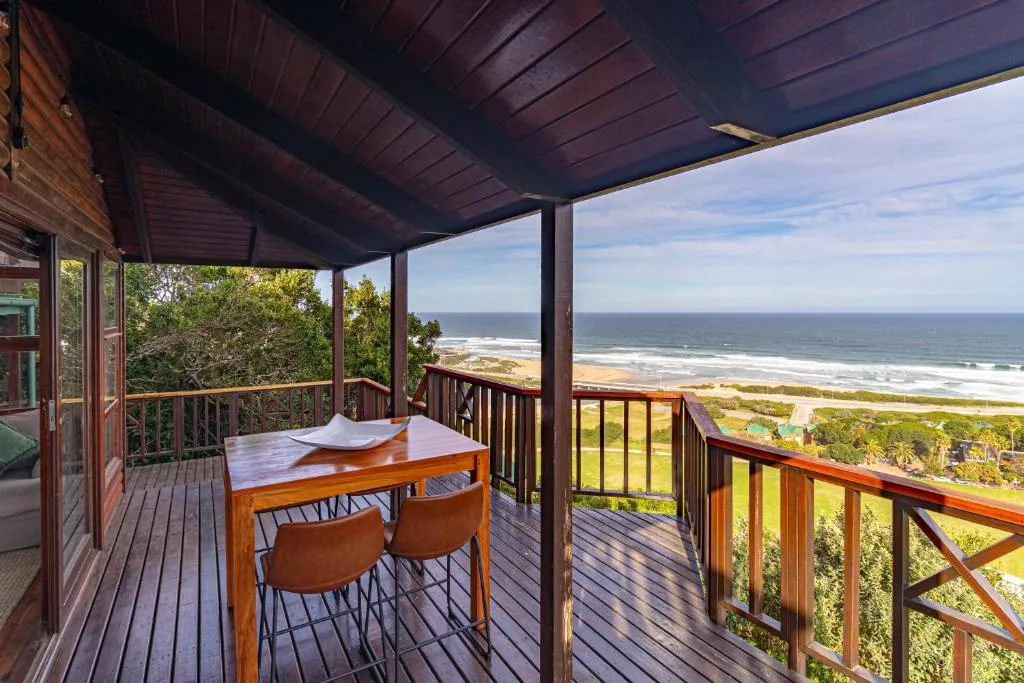 Covered wooden deck with dining table overlooking ocean and beach below