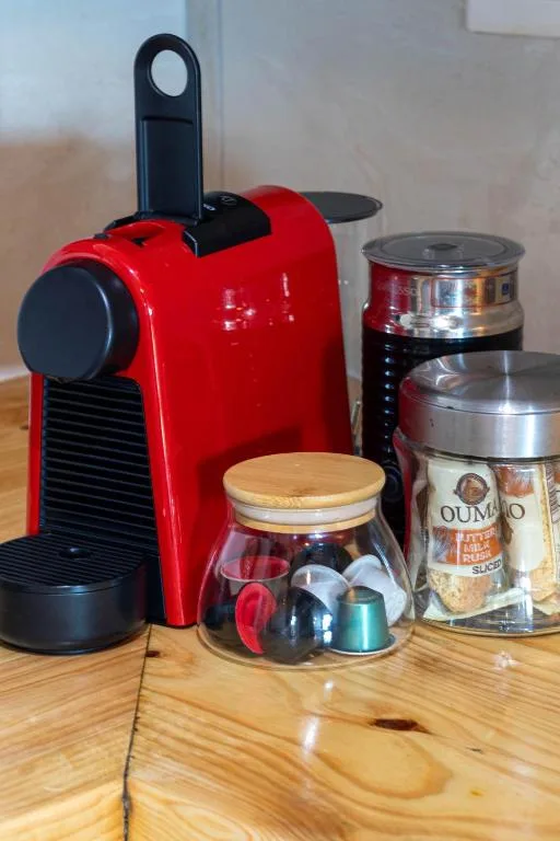 Red espresso machine with coffee capsules and storage containers on wooden counter