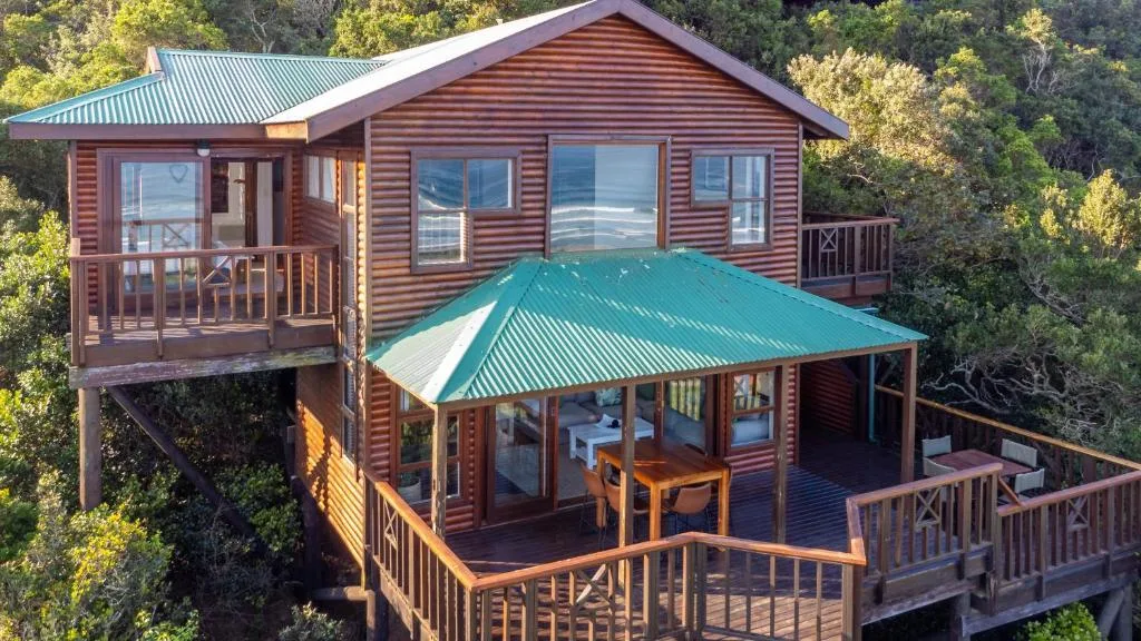 Red timber chalet with turquoise roof surrounded by indigenous forest vegetation