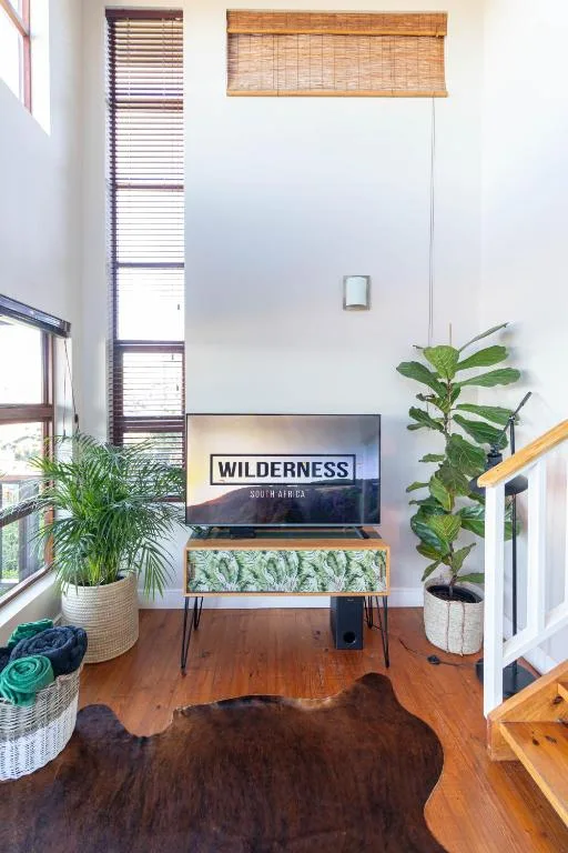 Bright lounge with TV, wooden floors, potted plants, and tall windows