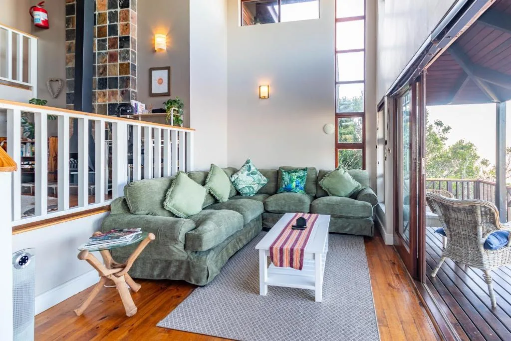 Spacious lounge with green sectional sofa and outdoor views through large doors