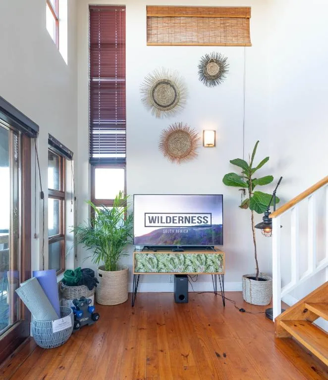 Modern lounge with TV, wooden floors, decorative wall baskets, and potted plants