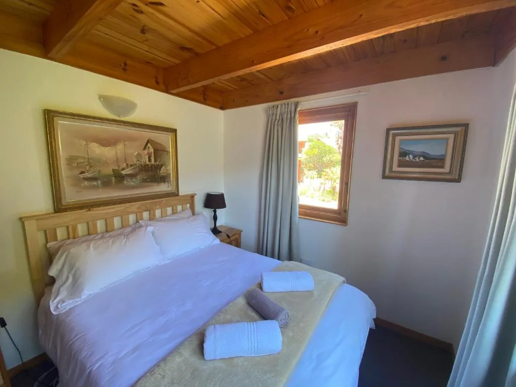 Bright bedroom with queen bed, wooden ceiling, framed artwork, and garden views