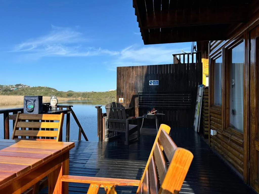 Waterfront deck with wooden furniture overlooking calm lagoon and hills