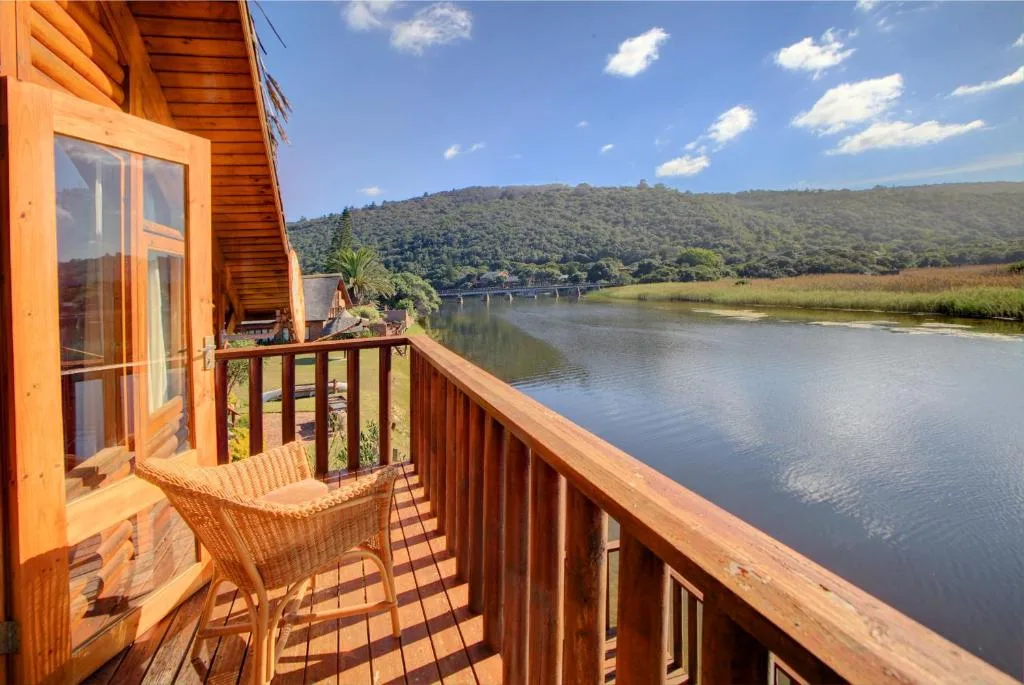 Wooden deck with chair overlooking river and forested mountains under blue sky