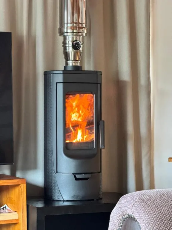 Modern wood-burning stove with active flames and metal chimney pipe