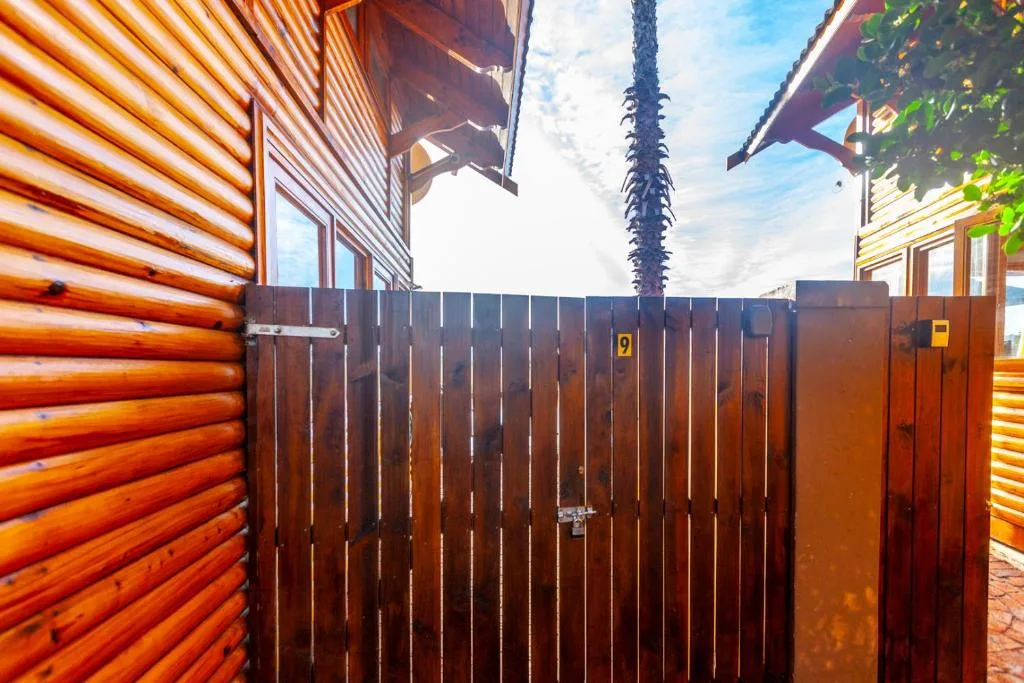 Wooden chalet entrance with dark metal gate and palm tree backdrop
