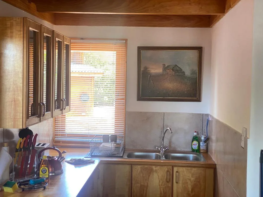 Compact kitchen with wooden cabinetry, sink, and window overlooking garden