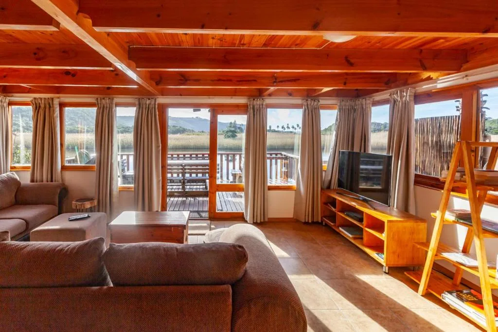 Spacious lounge with wooden beams, sofas, and expansive windows overlooking lagoon views