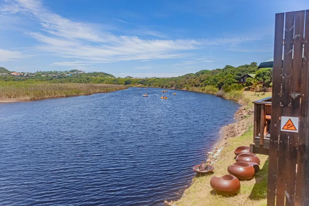 Scenic lagoon view with kayakers, lush vegetation, and rolling hills