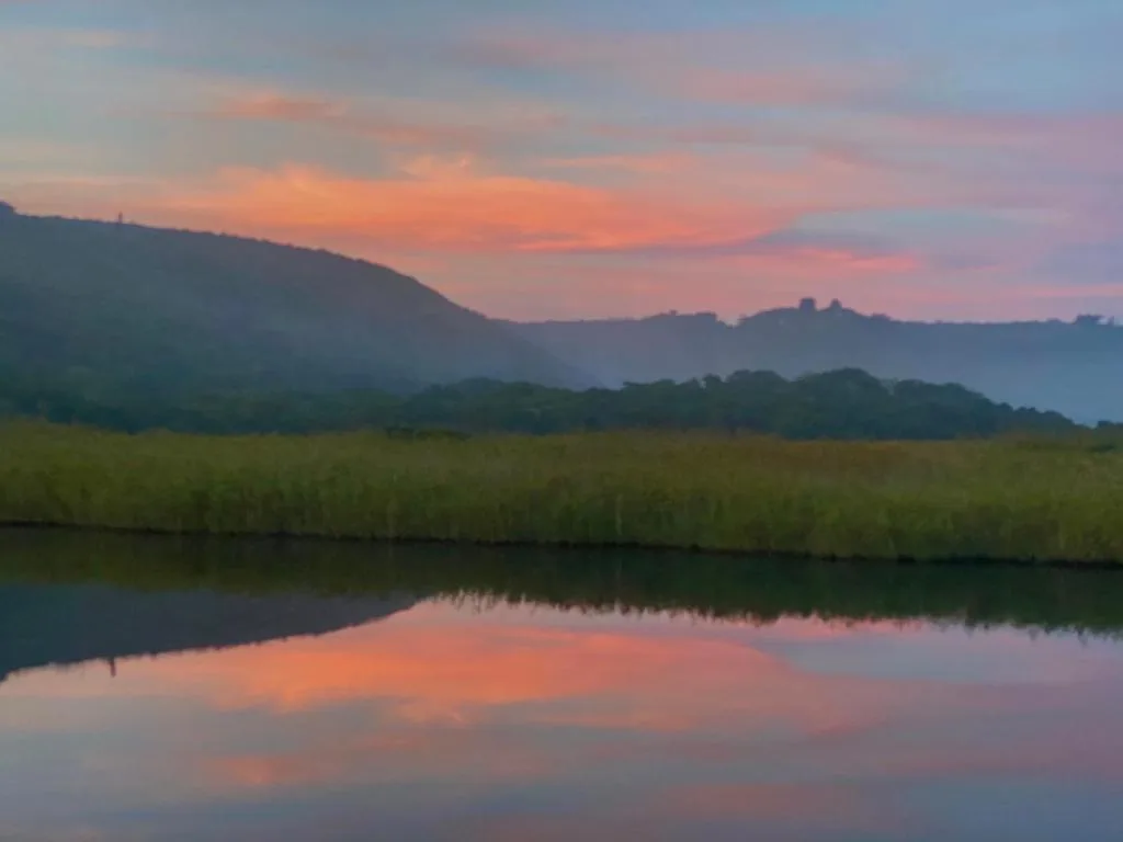 Sunset over lagoon with mountains and lush green vegetation reflected