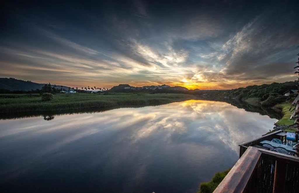 Stunning sunset over lagoon with mountains and dramatic cloudy sky reflected in water