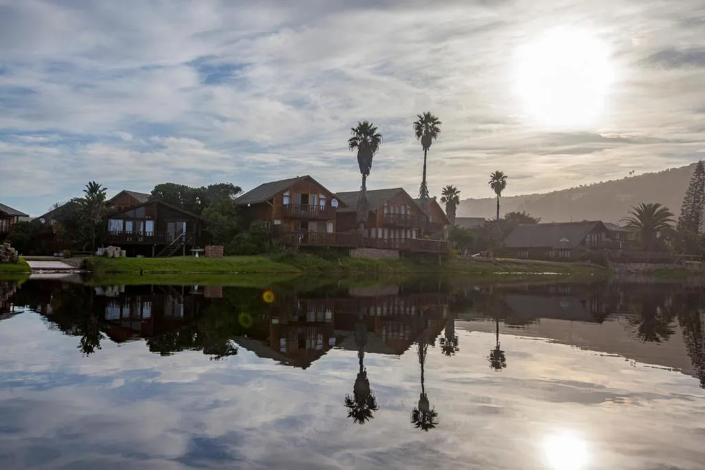 Waterfront cottages reflecting in still lagoon water with palm trees and mountains