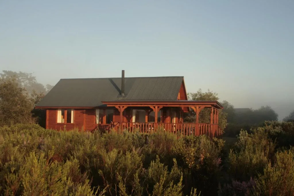 Red wooden cottage with wraparound porch nestled in fynbos vegetation