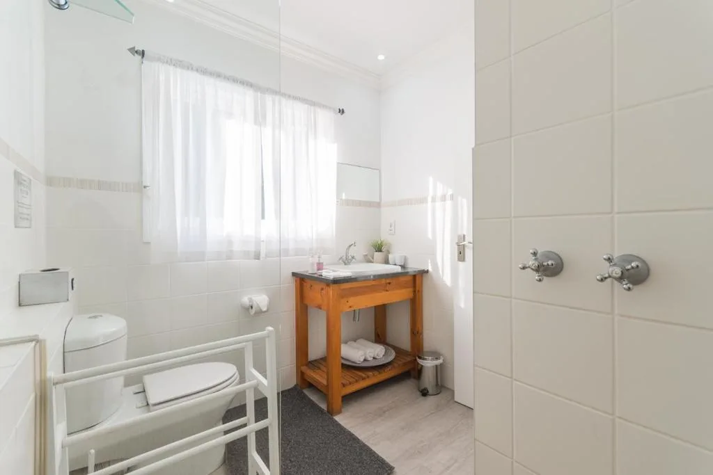 Bright bathroom with wooden vanity, toilet, heated towel rail, and shower area