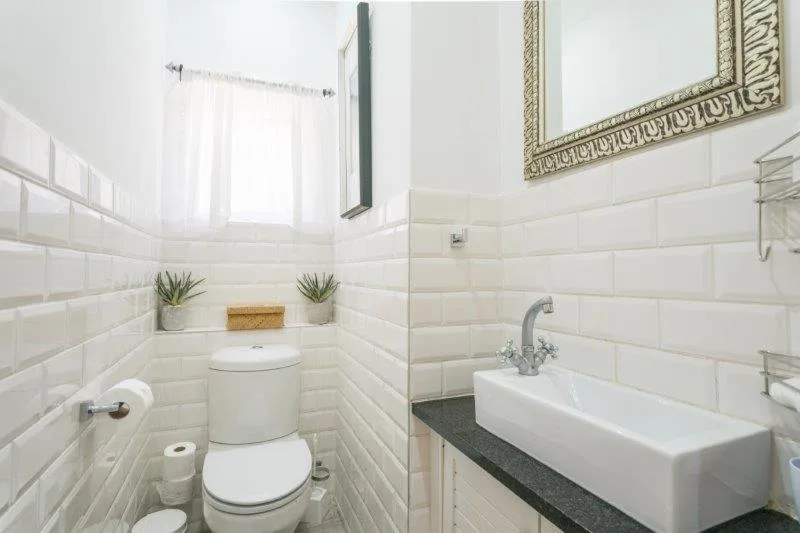 Modern bathroom with white subway tile, toilet, pedestal sink, and decorative mirror