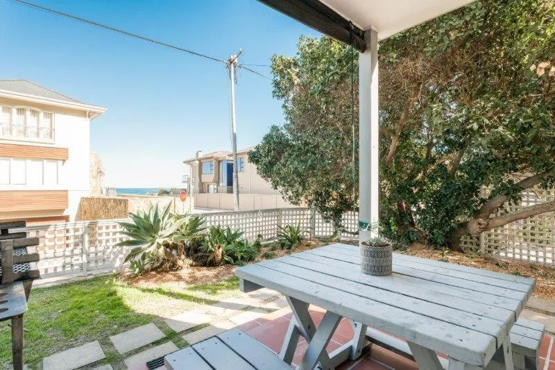 Shaded outdoor patio area with wooden table and ocean views nearby