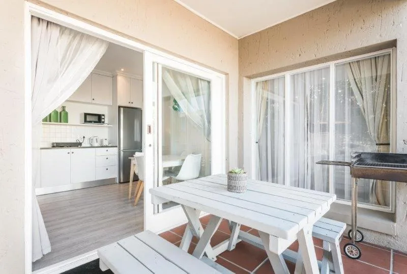 White wooden dining table on covered deck with braai and garden views