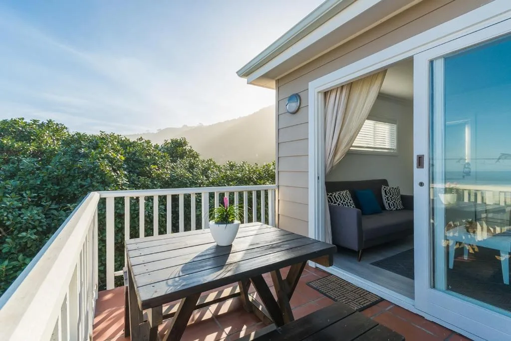Sunny wooden deck with white railing, table, and ocean view beyond