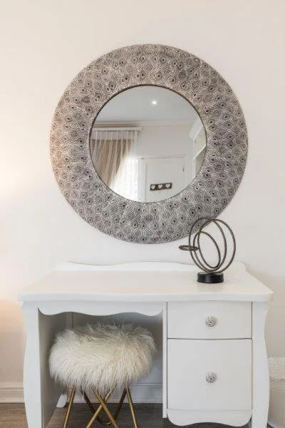 Decorative round mirror above white vanity desk with chair