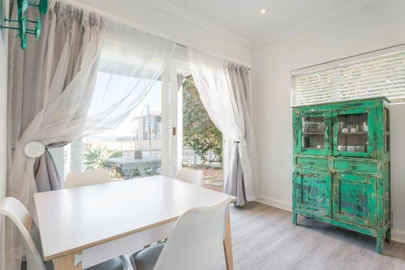 Bright dining area with white table, green vintage cabinet, garden views
