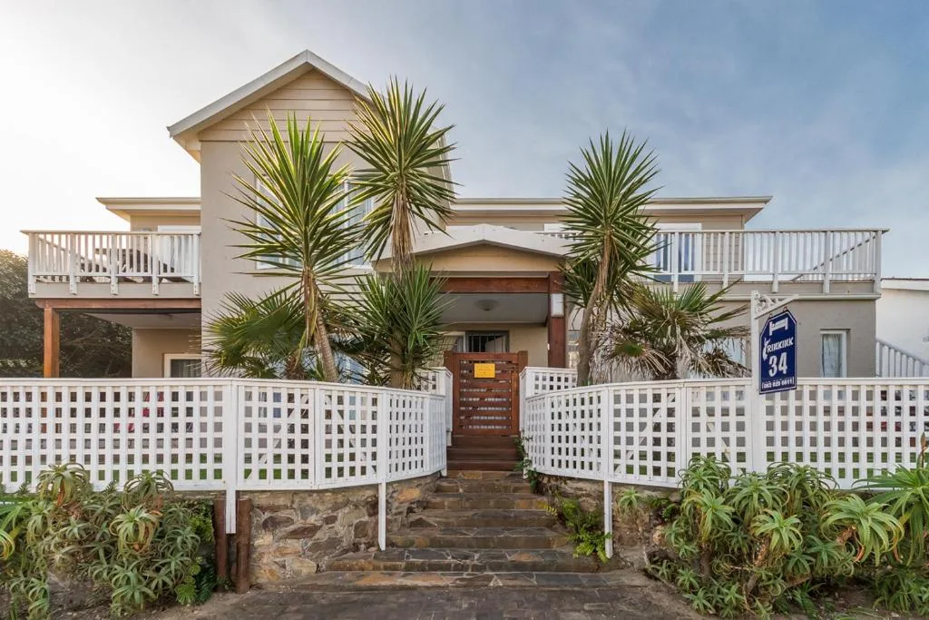 Modern beachfront house with white railings and palm trees at entrance