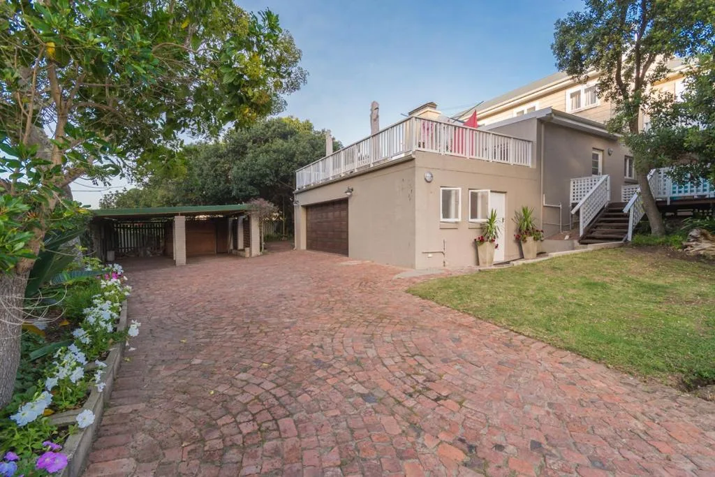 Beige residential building with brick driveway, garden, and wooden deck above
