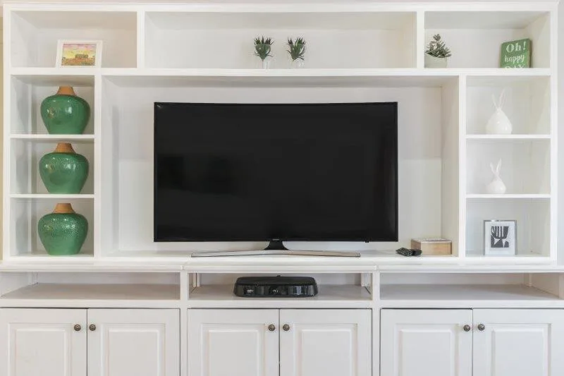Built-in white shelving unit with TV and decorative green ceramic vessels