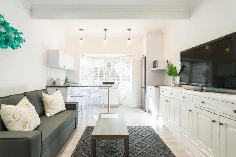 Open-plan lounge with grey sofa, TV, and kitchen area visible
