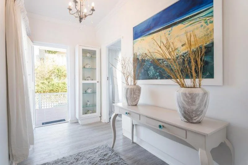 Bright lounge with white furniture, coastal artwork, and garden view access