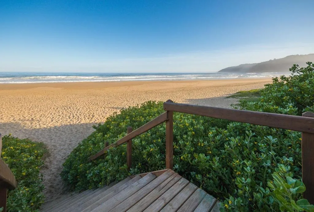 Expansive sandy beach and ocean view from wooden deck with railing
