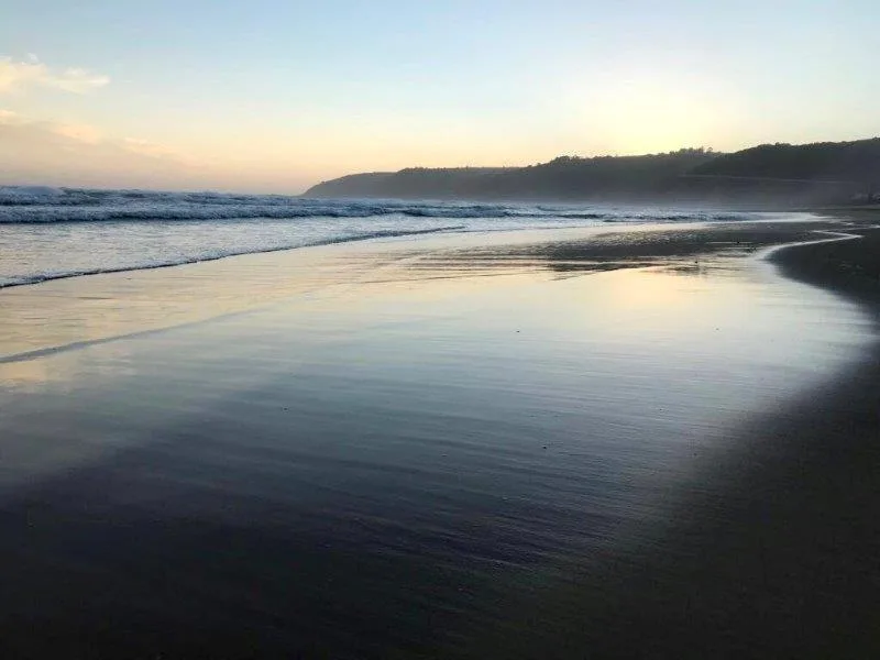 Serene beach at dawn with calm lagoon waters and forested cliffs