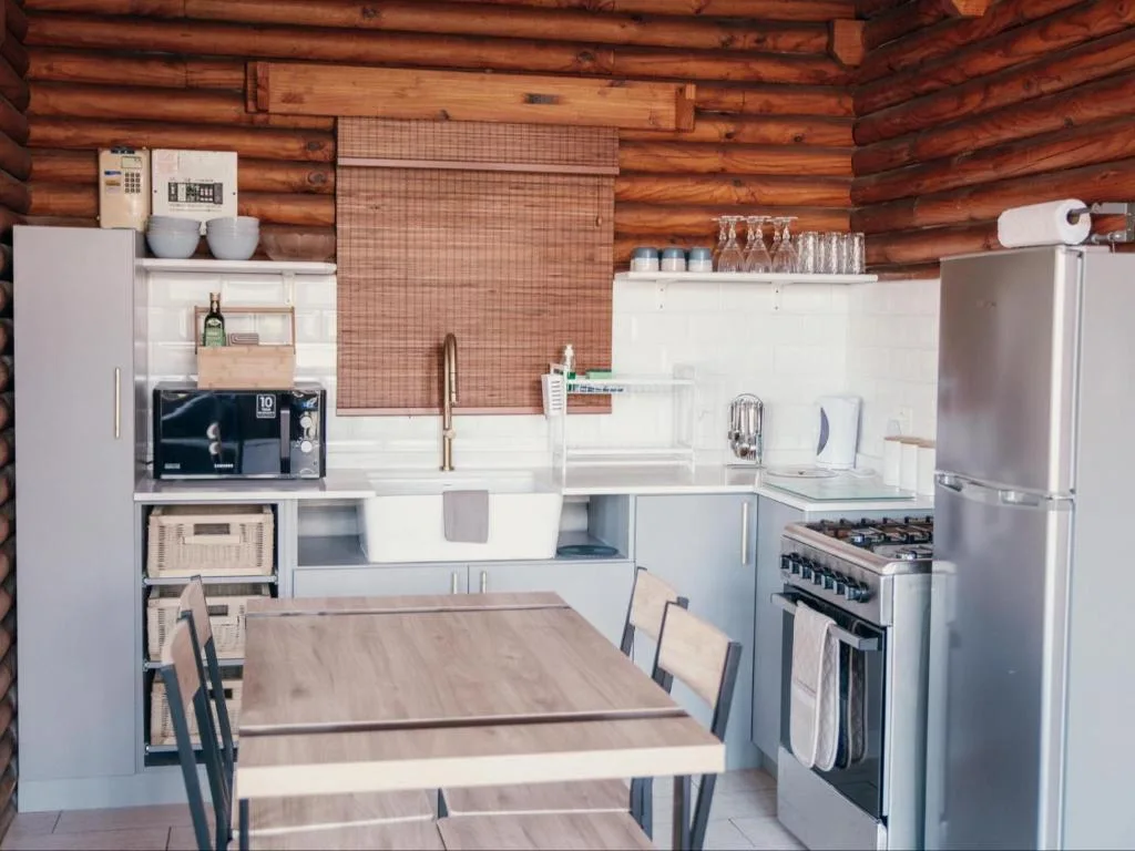 Modern kitchen with stove, refrigerator, and dining table in log cabin