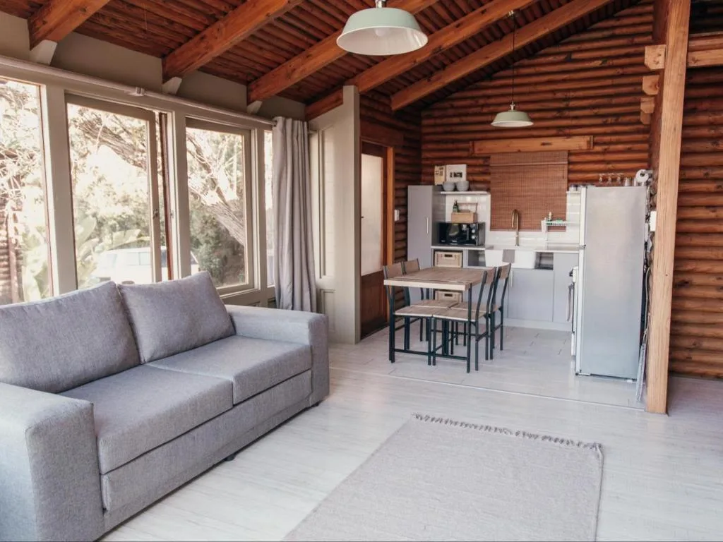 Open-plan lounge with gray sofa, wooden beams, and kitchen area visible beyond