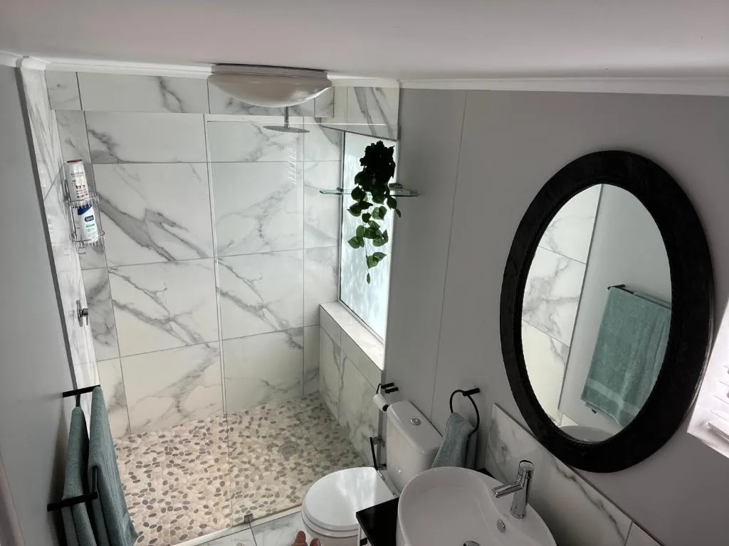 Modern bathroom with marble-tiled shower, round black mirror, and white vanity.