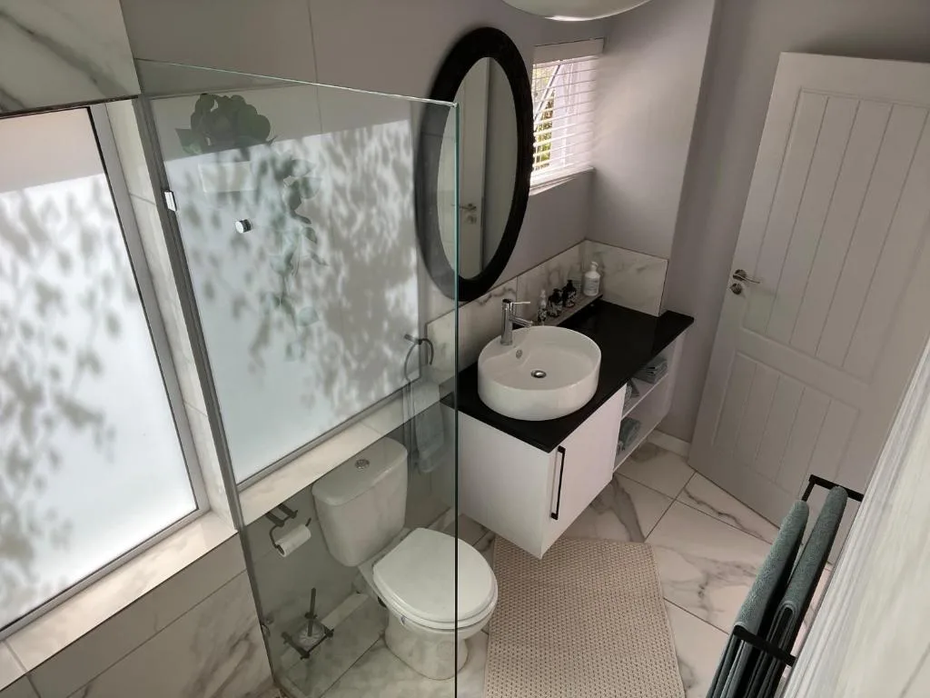 Modern bathroom with glass shower enclosure, round mirror, and white vanity sink